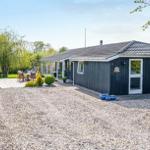 A house with dark siding, patio, and garden. A car is parked on the gravel drive.