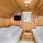 Two beds with white bedding, wooden walls, and a window.
