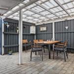 Terrace with seating under glass roof, paved and with walls of dark wood.