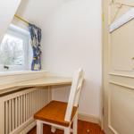 Schreibtisch mit Stuhl unter Fenster, Tür mit Schild und Heizkörper.