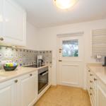 Küche mit weißen Schränken, blau-weißem Fliesenspiegel und integriertem Backofen.