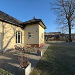 Haus mit Terrasse, Tisch und Stühlen, Rasenfläche und Baum im Hintergrund.