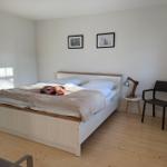 Schlafzimmer mit Bett, Stuhl und Lampe an der Wand.