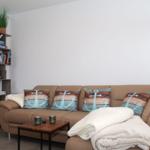 Ein Sofa mit Kissen und Decke. Bücherregal mit Dekoration.
