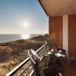 Terrasse mit Meerblick, Tisch und Stühle, Sonne scheint über dem Meer.