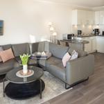 Wohnbereich mit Sofa, Couchtisch und Küche im Hintergrund.