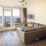 Wohnzimmer mit Sofa, Terrasse und Meerblick durch große Fenster.