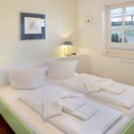 Zwei Betten mit weißen Laken und Handtüchern. Fenster mit Blick nach draußen.