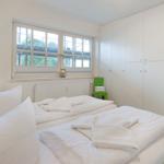 Schlafzimmer mit Doppelbett, weißen Wänden und großen Fenstern.