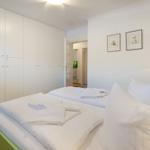 Schlafzimmer mit weißem Bett, Kleiderschrank und Nachttisch mit Lampe.