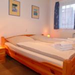 Ein Schlafzimmer mit Holzbett, Nachttisch und Fenster mit Vorhängen.