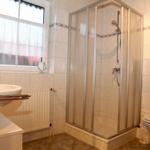 Badezimmer mit Dusche, Waschbecken und Toilette. Fenster mit Vorhang.