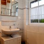 Badezimmer mit Waschbecken, Spiegel und Fenster mit Vorhang.