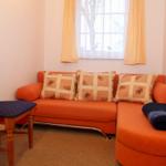 Orange Sofa mit Kissen und Decke vor Fenster mit Vorhängen.