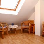 Zimmer mit Dachschrägen, Rattanstühlen, Tisch und Schubladenregal unter Dachfenster.