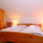 Ein Schlafzimmer mit Holzbett, Nachttischen und Kleiderschrank unter Dachschrägen.