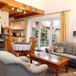 Wohn- und Essbereich mit Sofa, Couchtisch und Holzdecke. Durchgang zur Küche und Terrasse.