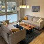 Wohnzimmer mit zwei Sofas, Holztisch und großen Fenstern.