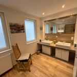 Badezimmer mit zwei Waschbecken, Spiegeln und Holzboden. Holzstuhl und Fenster sichtbar.