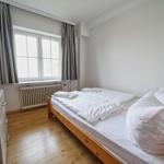 Schlafzimmer mit Bett, Kleiderschrank und Fenster mit Vorhängen.