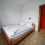 Schlafzimmer mit Bett, Holzboden und roter Türvorhang.