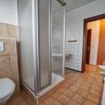 Badezimmer mit Dusche, Toilette und Waschbecken. Fliesenboden und -wände.