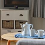 Tisch mit Teekanne und Tassen, Fernseher und Schrank im Hintergrund.