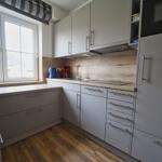 Küche mit hellen Schränken, Holzboden und Fenster mit Blick nach draußen.