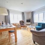 Wohn- und Essbereich mit Holzboden, Sitzgelegenheiten und Fenstern.