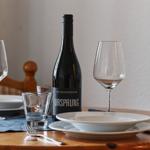 Tisch gedeckt mit Weinglas, Flasche und Geschirr.