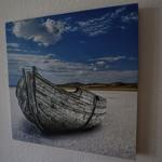 Ein altes Boot liegt auf einer salzhaltigen Fläche unter einem blauen Himmel mit Wolken.