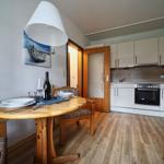 Essbereich mit Tisch und Stühlen, Küche mit Dunstabzug und Herd, Holzboden und Wandbild.