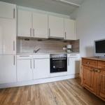 Küche mit weißen Schränken, Holzboden und TV-Schrank