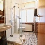 Badezimmer mit Dusche, Waschbecken und Toilette. Fliesenboden und Fenster.