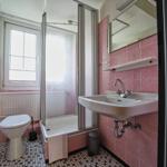 Badezimmer mit Dusche, Waschbecken und Toilette. Wandfliesen rosa, Bodenfliesen schwarz-weiß.