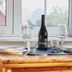 Tisch mit Weinflasche und Gläsern vor Fenster mit Bergblick