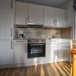 Küche mit weißen Schränken, Herd und Holztisch.