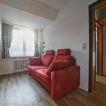 Ein Wohnzimmer mit rotem Sofa, Holzboden und Fenster mit Vorhängen.