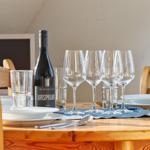 Gedeckter Holztisch mit Weinglas, Wasser und Weinflasche.