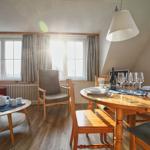 Ein Raum mit Esstisch, Sofa und Fenstern. Sonne fällt durch die Fenster.