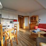 Wohnküche mit Essbereich, rotem Sofa und Holzmöbeln.