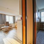 Wohnzimmer mit Sofa, Sessel und Fenstern. Nebenraum mit Fliesenboden und Fenster.