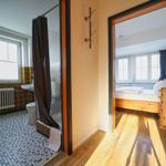 Badezimmer mit Dusche und Toilette. Nebenraum mit Bett und Holzboden.