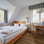 Schlafzimmer mit Bett, Tisch und Stühlen. Fenster mit Blick auf Bäume.