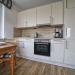 Küche mit Essplatz, weißen Schränken und Holzboden. Fenster mit Blick nach draußen.