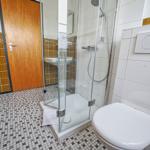 Badezimmer mit Dusche, Toilette und Waschbecken. Fliesen und Mosaikboden.