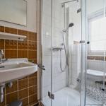 Bad mit Dusche, Waschbecken und Toilette. Fliesenwand und Fenster sichtbar.