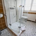 Bad mit Dusche, Toilette und Waschbecken. Fliesenboden und Fenster.