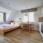 Schlafzimmer mit Bett, Essplatz und Küche. Holzboden und große Fenster.