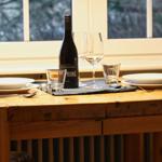 Holztisch mit zwei Platzsetzungen, Weinkrug und Fensterblick.